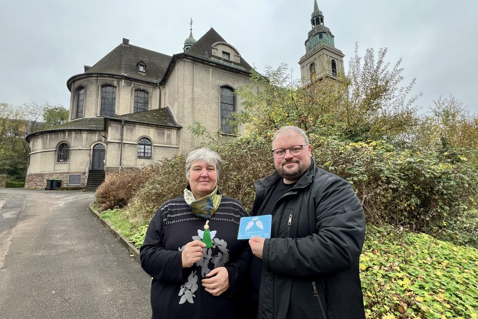 Zwei Menschen stehen vor einer Kirche und präsentieren eine Karte, die sie in der Hand halten