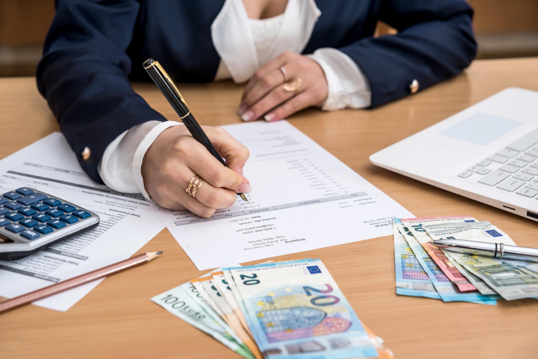 Frau die am Schreibtisch sitzt, Geld zählt und dabei Notizen macht