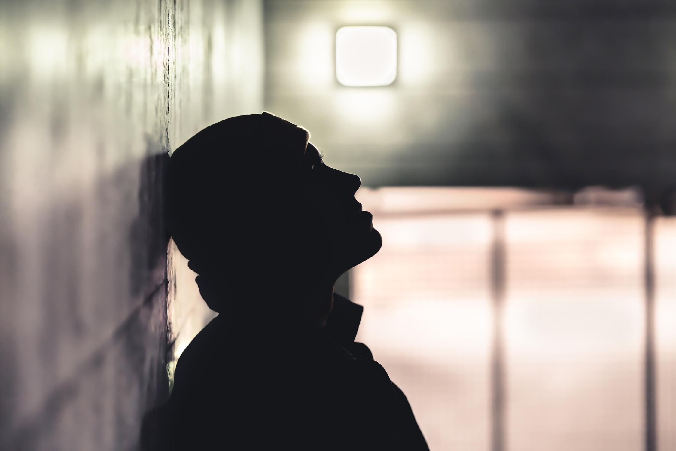 ein junger Mann mit Mütze, der im Schatten an einer Wand lehnt.